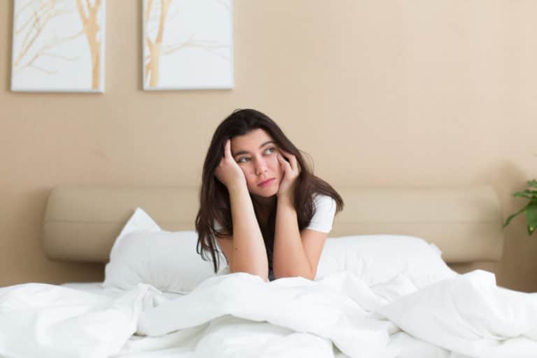 lady holding her face in bed suffering from migraine