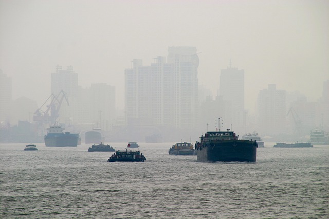 Boats and ocean in the foreground, with a heavy smog surrounding the city