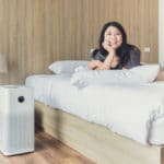 Lady on bed with an air purifier beside it