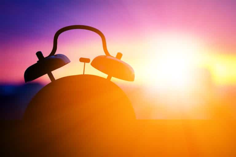 Silhouette of alarm clock with sunrise in the background