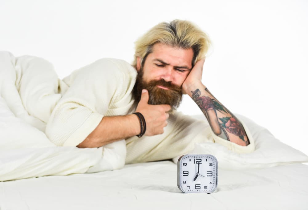 Man thinking in bed looking at alarm clock