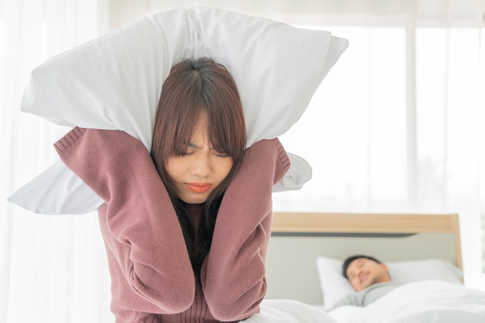 Wife covering ears with pillow due to snoring husband